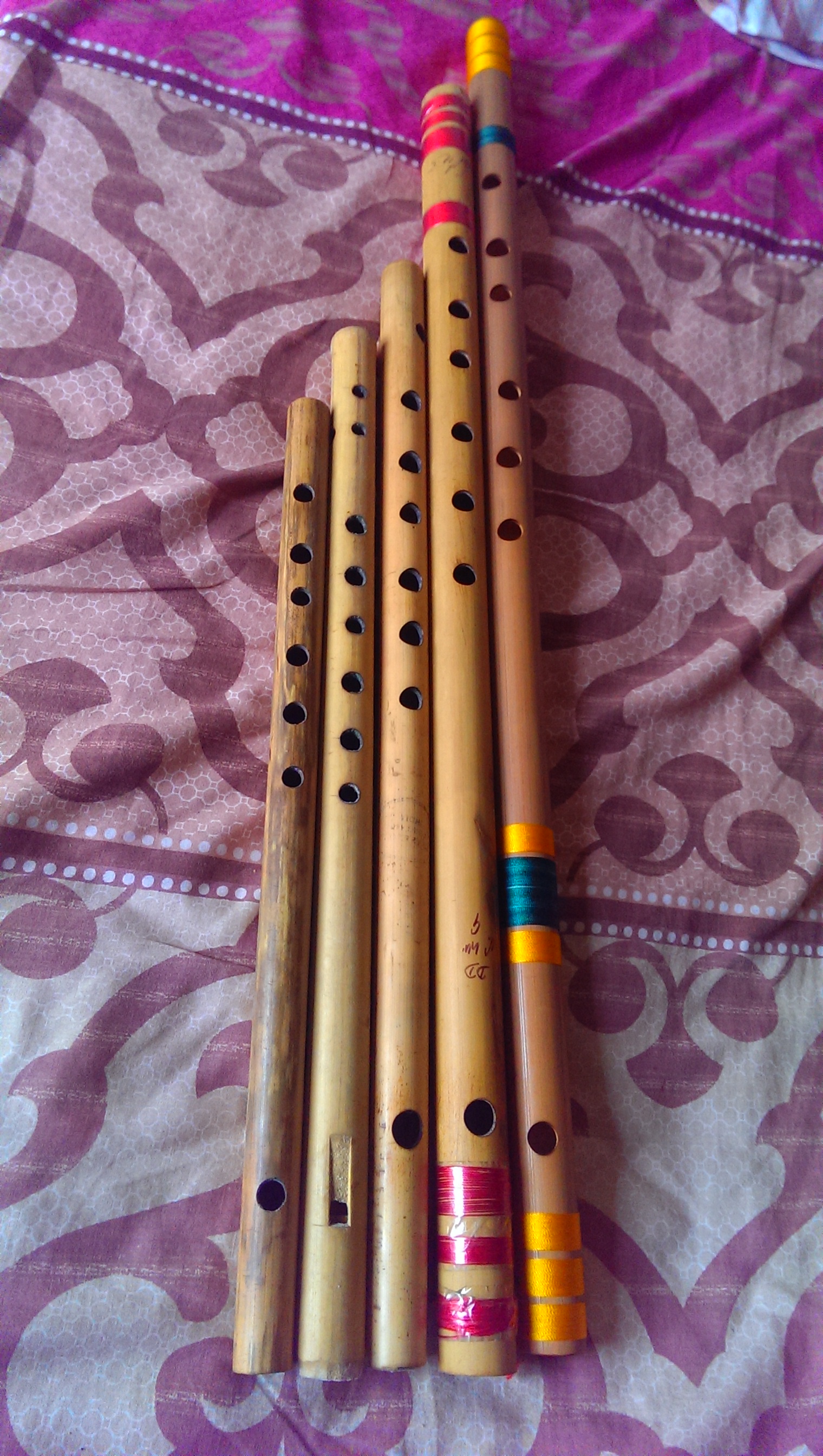 Five bamboo side-blown bansuri flutes of different lengths laid side by side.