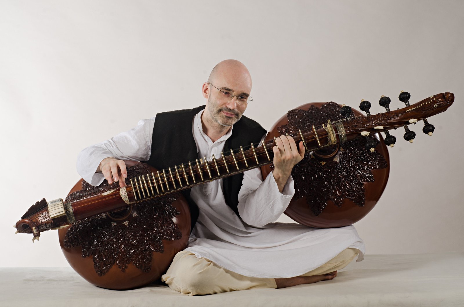 Carsten Wicke seated cross-legged holding a carved rudra veena