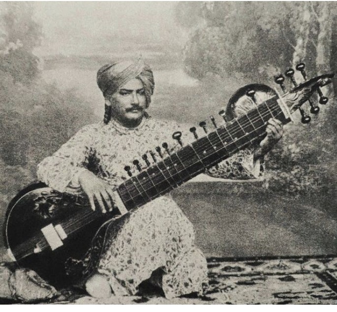 Seated musician in a turban and brocade coat holding a surbahar before a painted backdrop