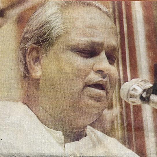 Close photograph of Kumar Gandharva singing at a microphone, a tanpura behind him.