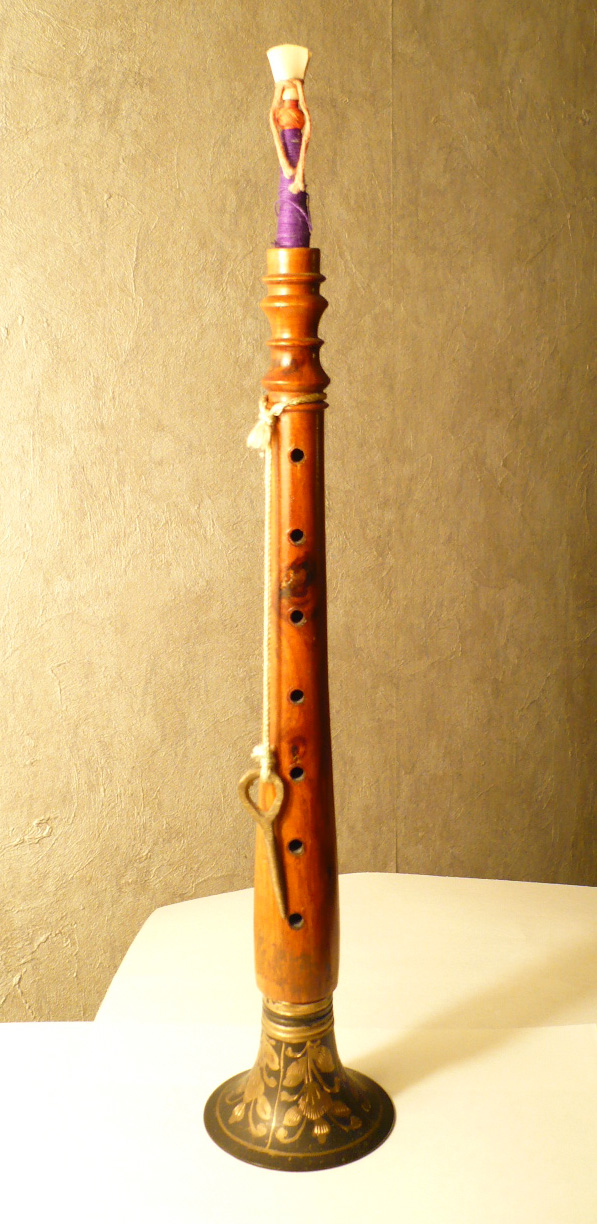 A shehnai standing upright, showing its conical wooden body and flared bell.
