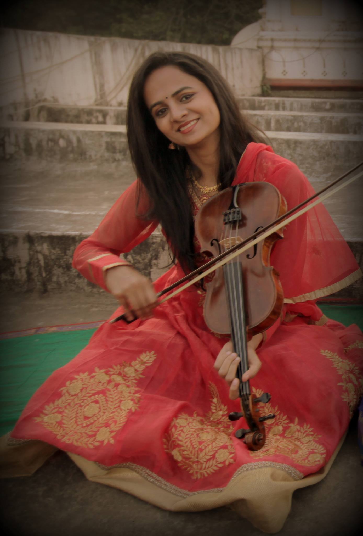 A seated violinist playing a violin held downwards in the Indian seated position.